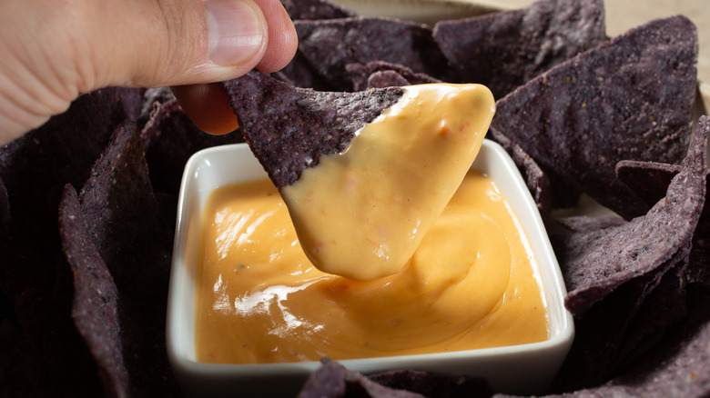 Someone dipping a blue corn chip into yellowy orange queso dip