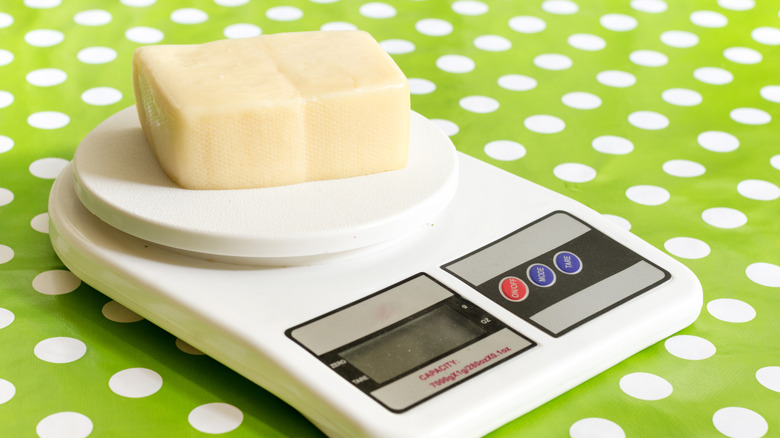 A small brick of white cheese sitting on a kitchen scale atop a green and white polka dot tablecloth