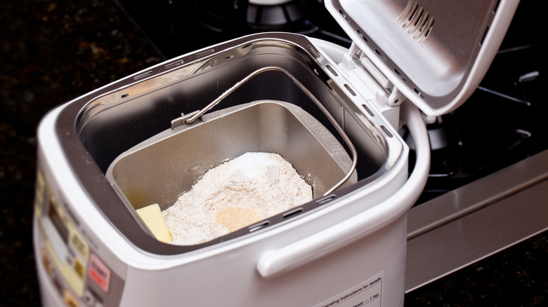 picture of a compact white bread machine with its lid open, revealing the flour, butter and other ingredients inside its pan