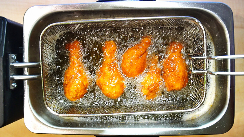 overhead view of a compact countertop deep fryer, with five small chicken drumsticks or wing "drumettes" turning golden brown in the hot oil