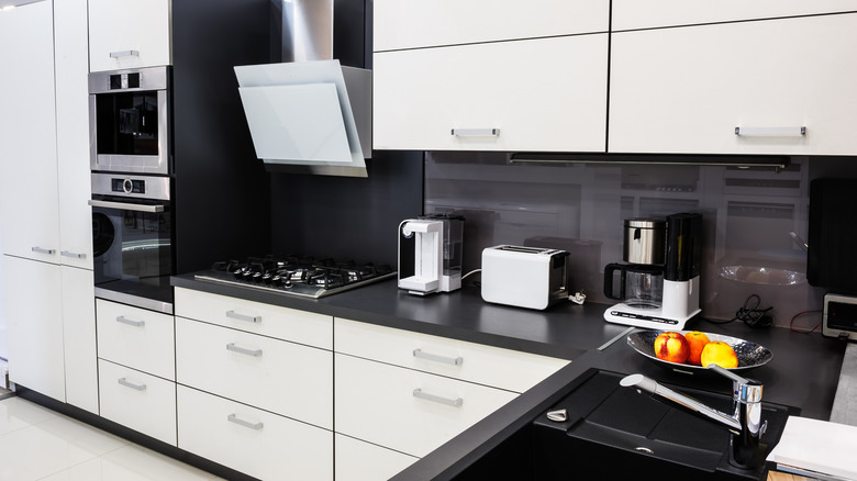 a sleek, modern kitchen in black and white, with a few countertop appliances on the black stone-look counter
