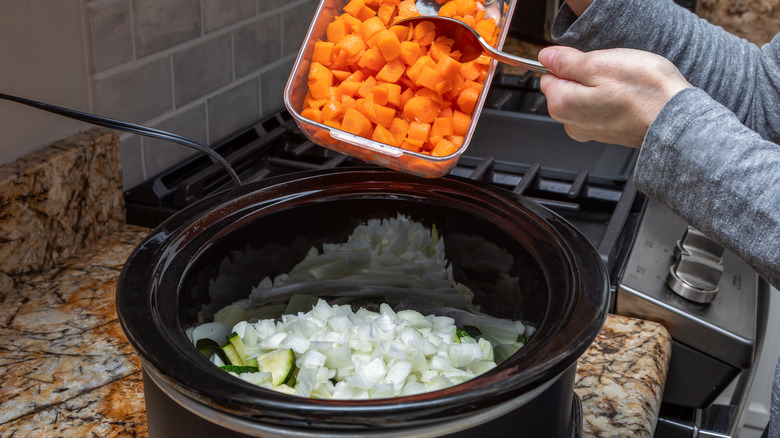a woman's gray-clad arms shown dumping a container of chopped carrots into a slow cooker