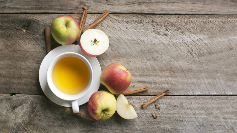 A tea cup surrounded by fresh apples and cinnamon sticks