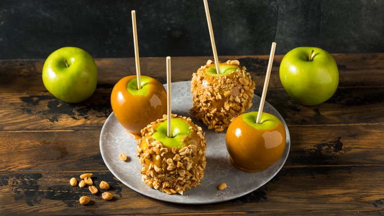 Green caramel apples rolled in chopped nuts on gray plate next to whole apples