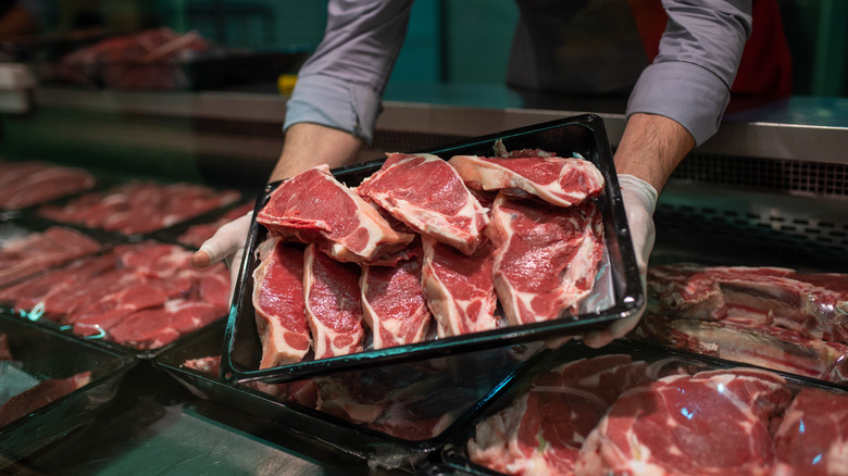 Butcher placing tray of steaks in case with other steaks.