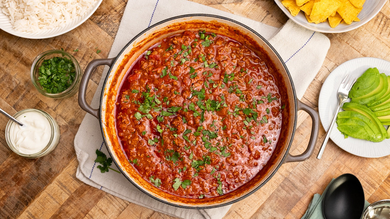 Aerial view of West Texas chili in pan surrounded by sliced avocado, tortilla chips, and rice