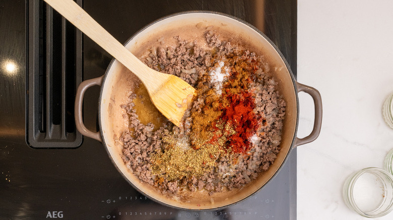 A pan with cooked beef and various spices sprinkled on top
