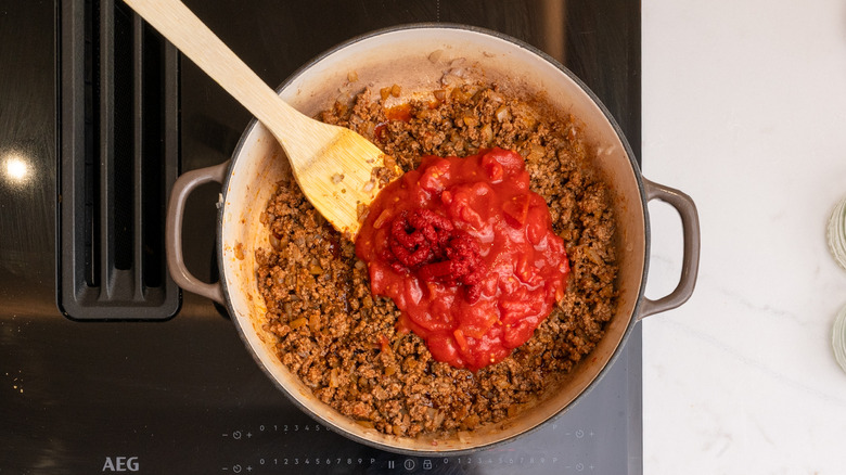 Canned tomatoes, tomato paste, and amber ale added to a pan with cooked beef and onions
