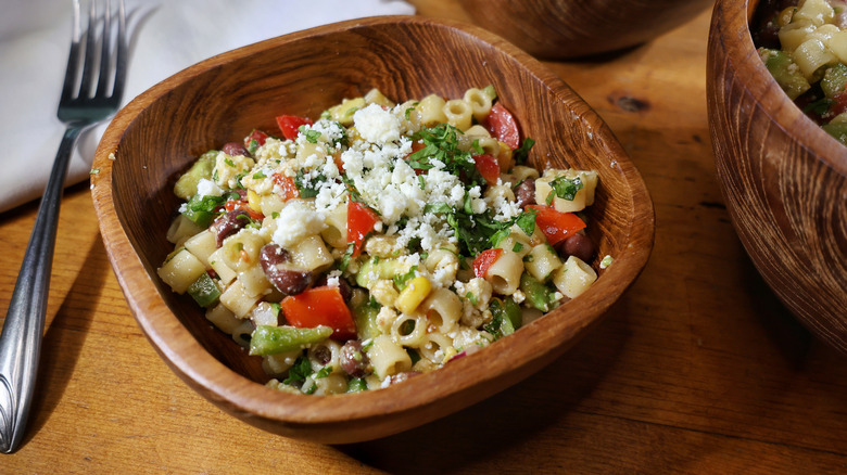 a wooden bowl of cowboy caviar pasta salad with a fork and napkin beside it on a wooden table