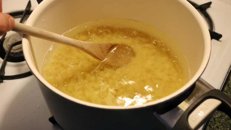 wooden spoon stirring pot of cooking ditalini pasta