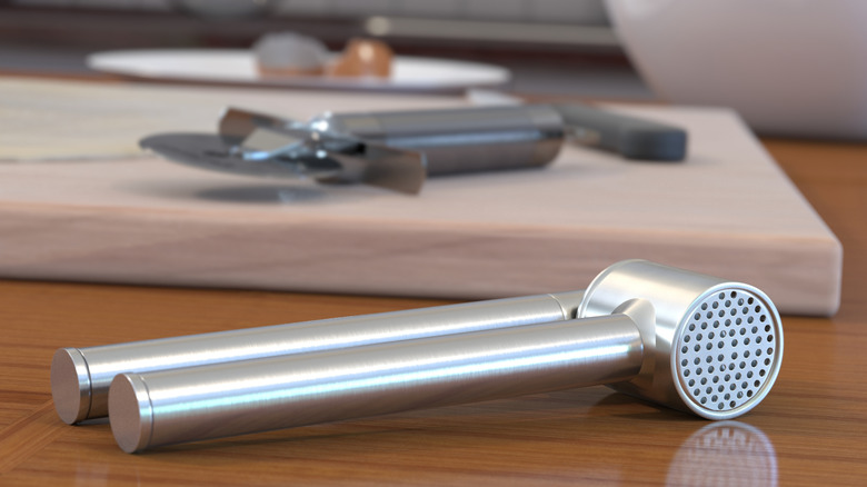Garlic press with pizza slicer on cutting board