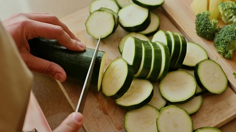 Home chef slicing zucchini on wooden cutting board.