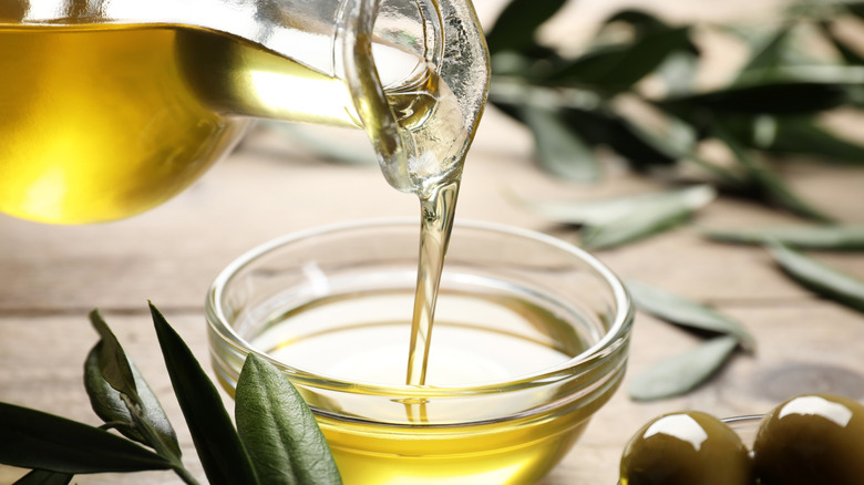 Glass jar of olive oil being poured into small glass bowl.