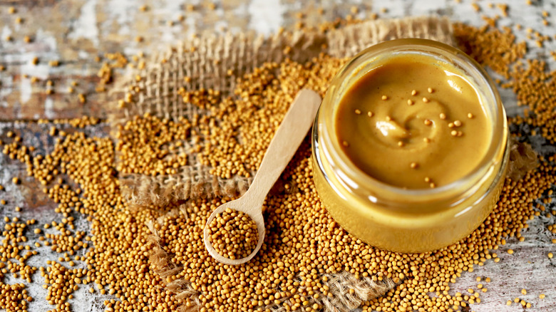 Jar of Dijon mustard surrounded by mustard seeds