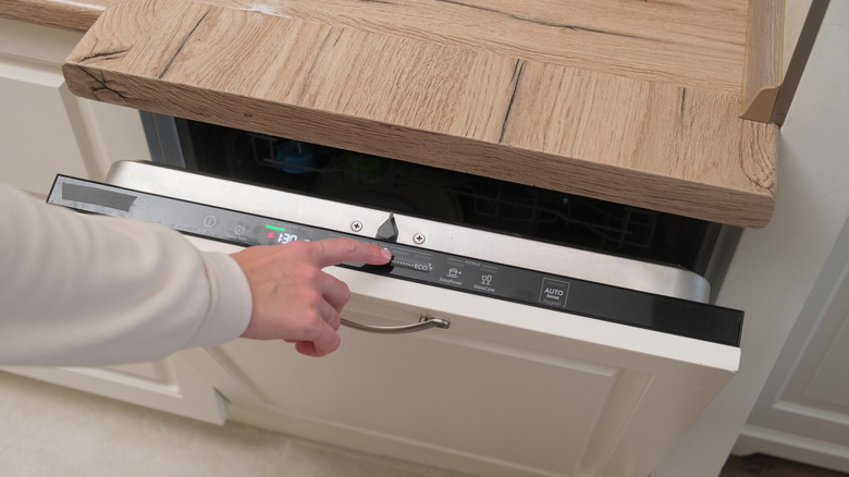 Finger about to close and turn on the dishwasher.