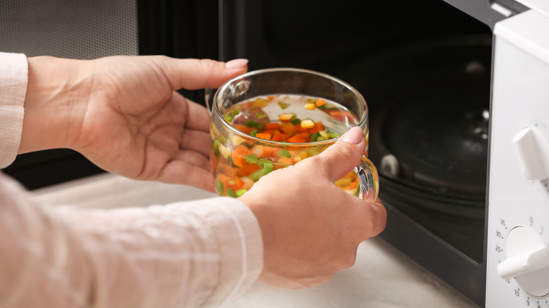 A person taking a defrosted mug of soup out of the mircowave