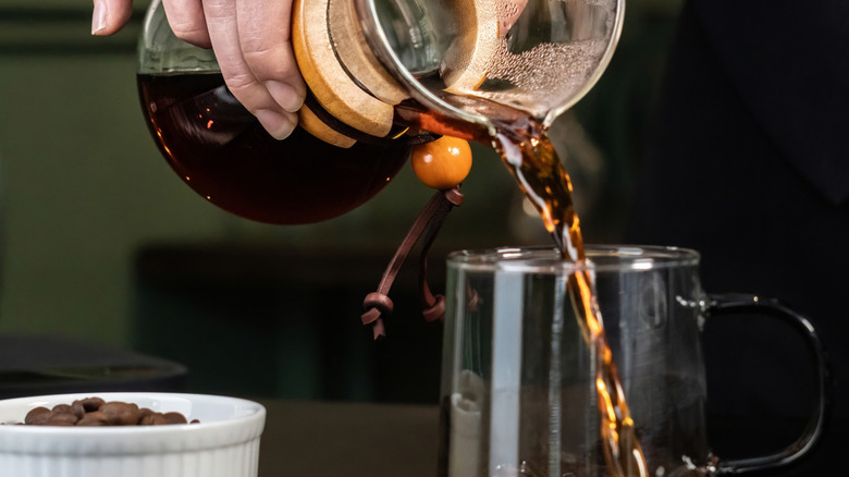 Someone pouring coffee into a glass mug from a Chemex