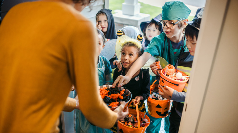 A group of costumed children clamor for Halloween candy while trick-or-treating at a home