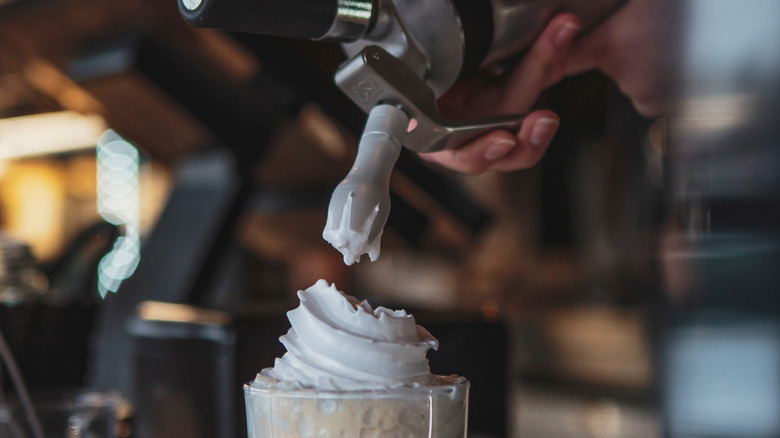 A bartender using a whipped cream dispenser to add whipped cream to an Irish coffee cocktail