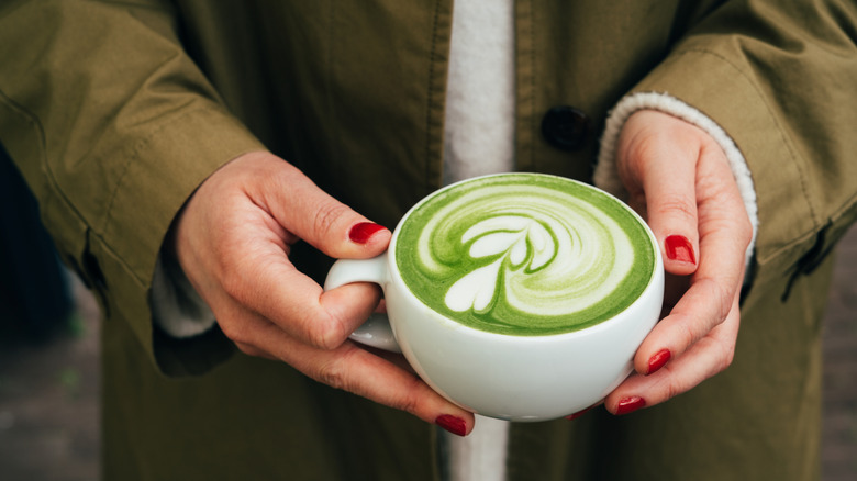 Person with red nails holding a cup of matcha latte