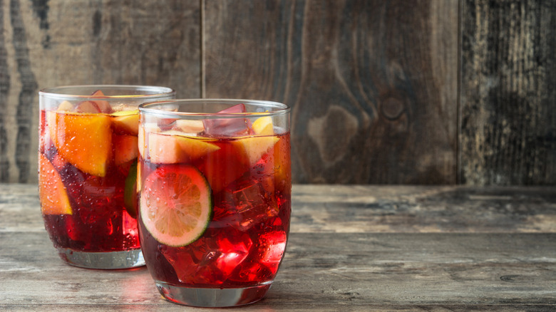 Two glasses of ice and fruit filled sangria against a wooden backdrop