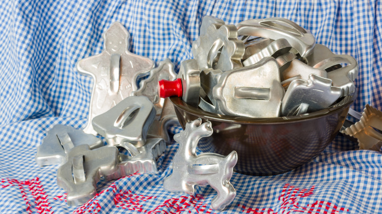 A bowl full of vintage aluminum Christmas shaped cookie cutters with some Spilled Out next to it on a blue Checker cloth