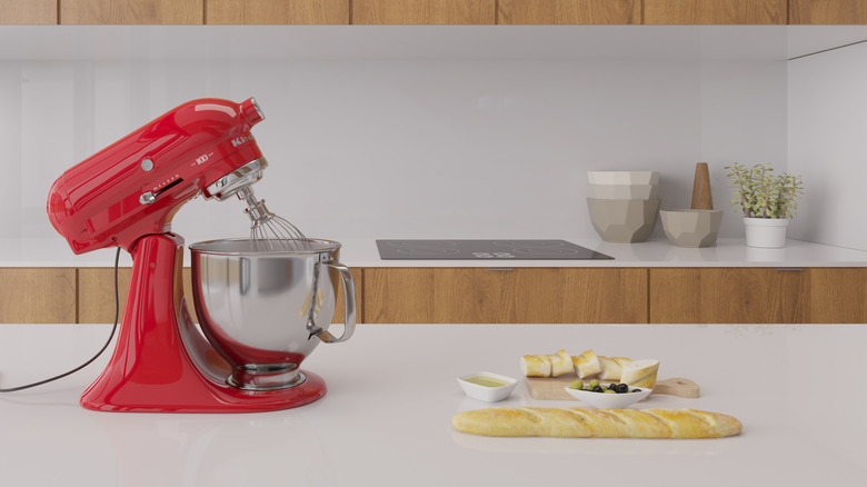 A red KitchenAid stand mixer on a kitchen counter next to a loaf of bread