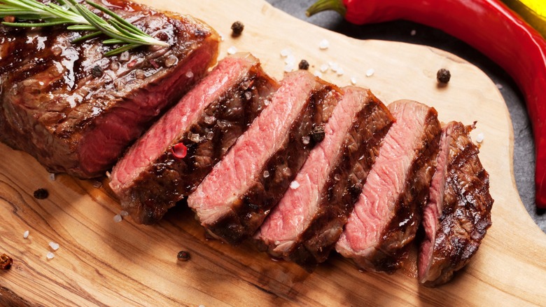 The grilled and sliced steak on a wooden board seasoned with some Rosemary, peppercorns, and salt