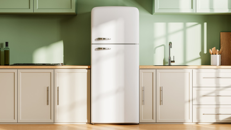 Retro-style white fridge in the center of a modern kitchen with green backsplash and cabinets