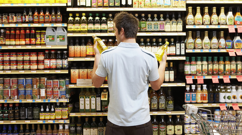 man in grocery store choosing between two types of olive oil.