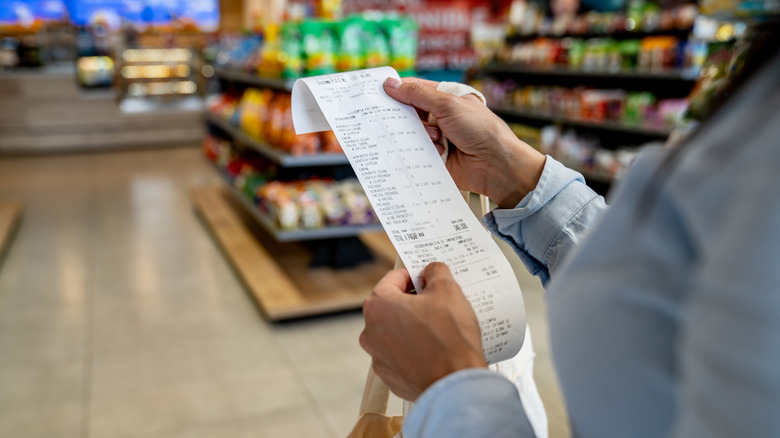 A woman standing in a grocery store looking at a long receipt.