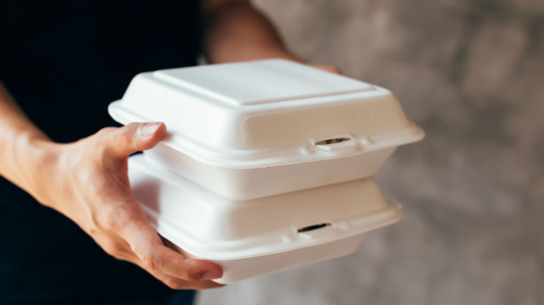 A person holding two styrofoam takeout containers