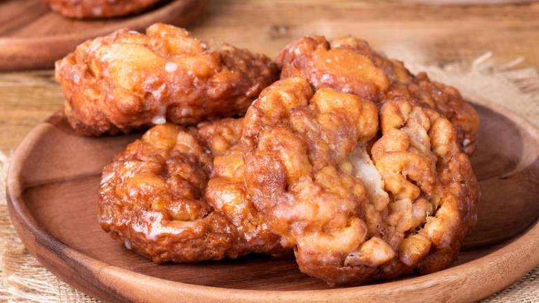 Four apple fritters with white glaze on wooden plate
