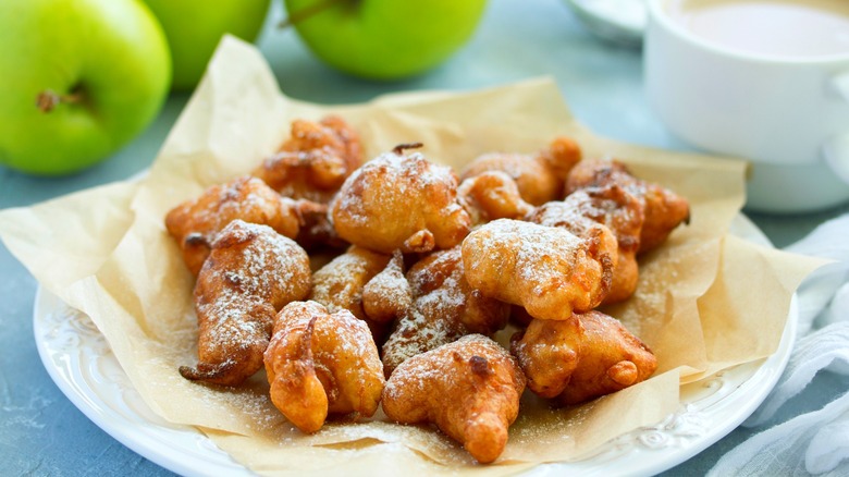 Plate of apple fritters dusted with powdered sugar next to whole green apples