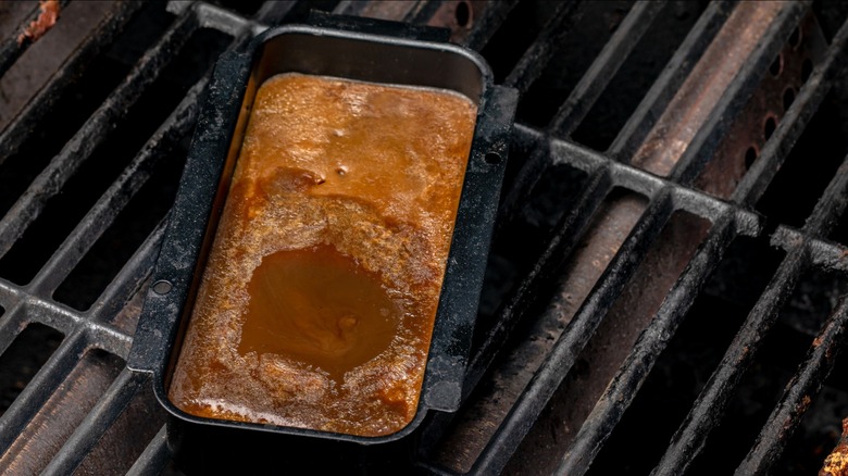 A drip pan full of grease sitting on top of the grates of a barbecue grill