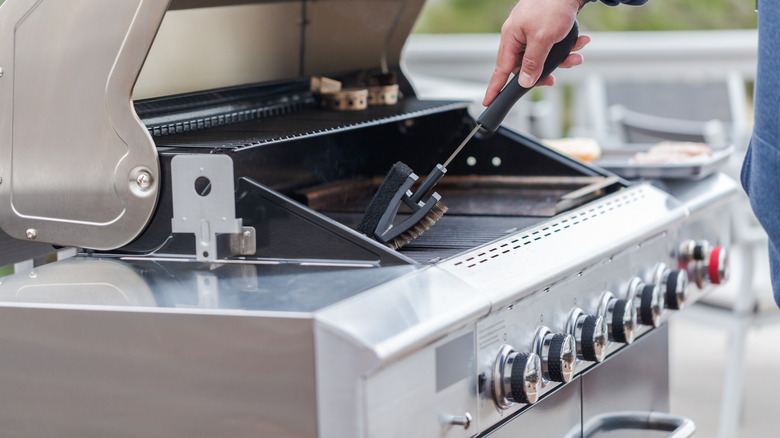 A hand cleaning a grill with a wire brush