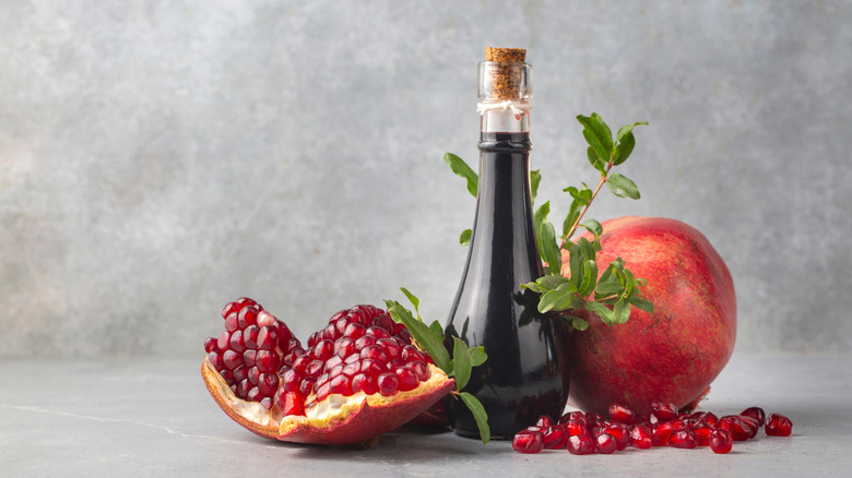 Bottle of homemade grenadine with a whole and halved pomegranate, next to seeds