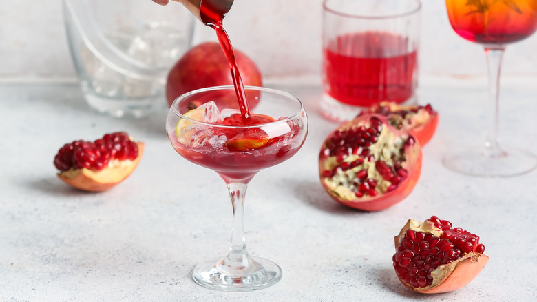 Adding grenadine to coupe glass surrounded by pomegranate