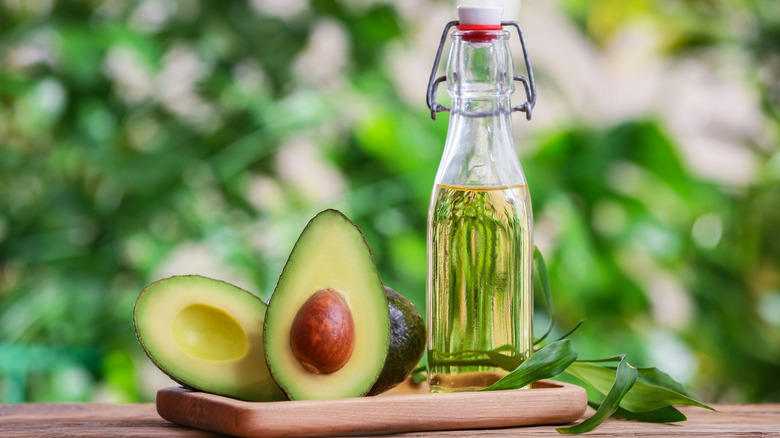 A bottle of avocado oil with avocado cut in half on a wooden board