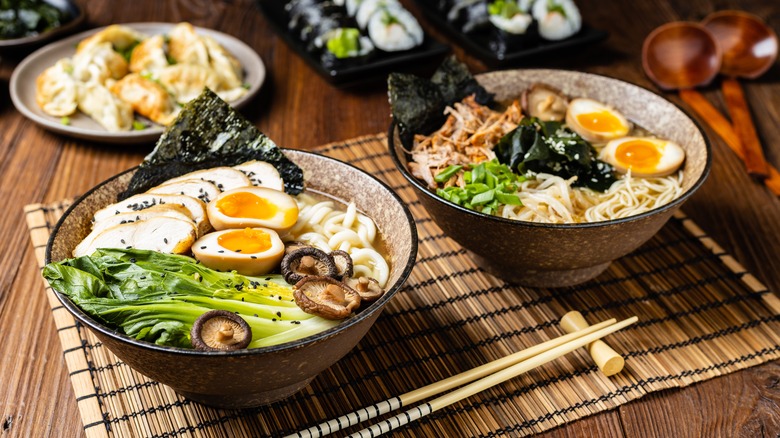 Ramen noodle  dishes with chopsticks and renge, and served with bamboo shoots, lime slices, greens, seafood and eggs