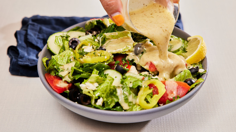 Creamy salad dressing pouring from a ramekin onto a bowl of salad